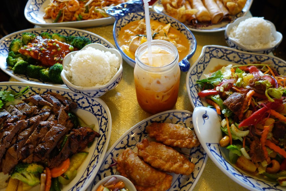 A table of Thai Garden dishes with curry, noodles, grilled meat and Thai iced tea